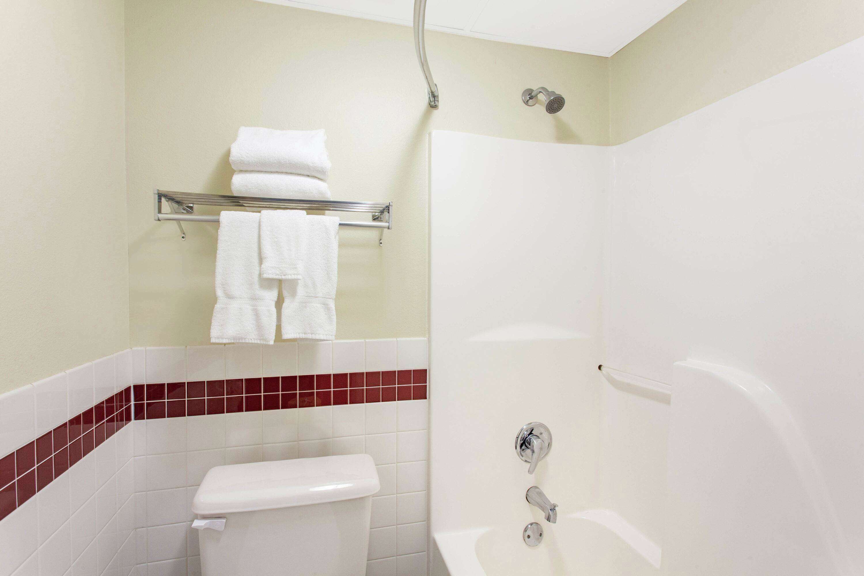 A bathroom with a toilet, a shower, and a bathtub. There is a towel rack with towels above the toilet.