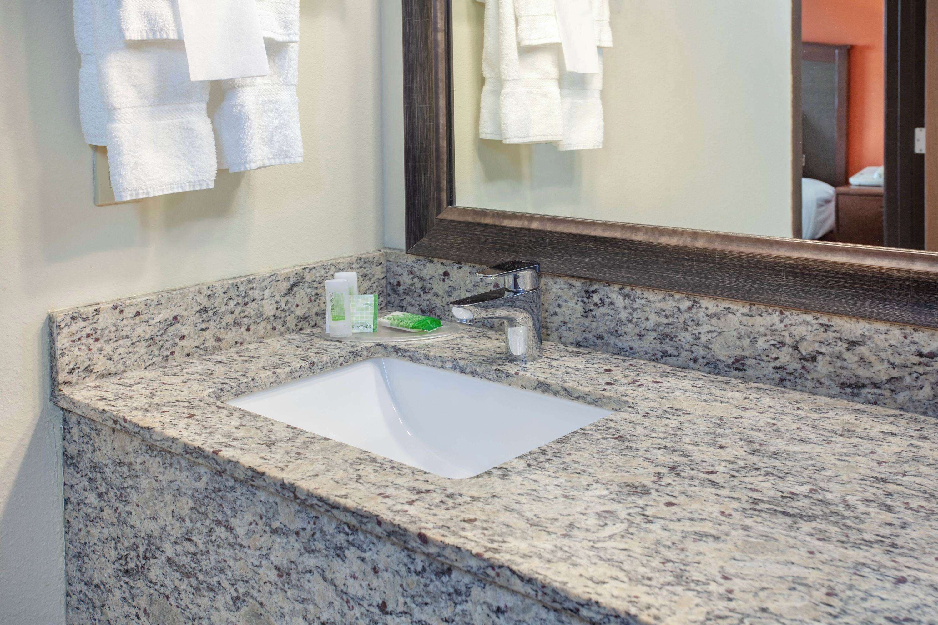 Une salle de bain avec un comptoir en granit, un lavabo blanc et un miroir.