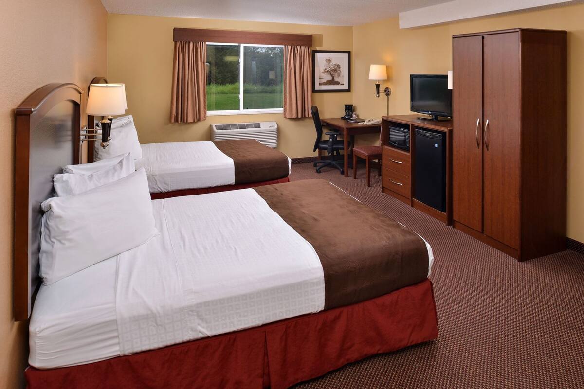 A hotel room with two beds, a desk with a computer, a television, and a wardrobe.