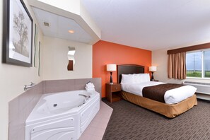 Habitación de hotel con una cama grande, baño independiente con bañera, dos lámparas de noche y una ventana con cortinas.