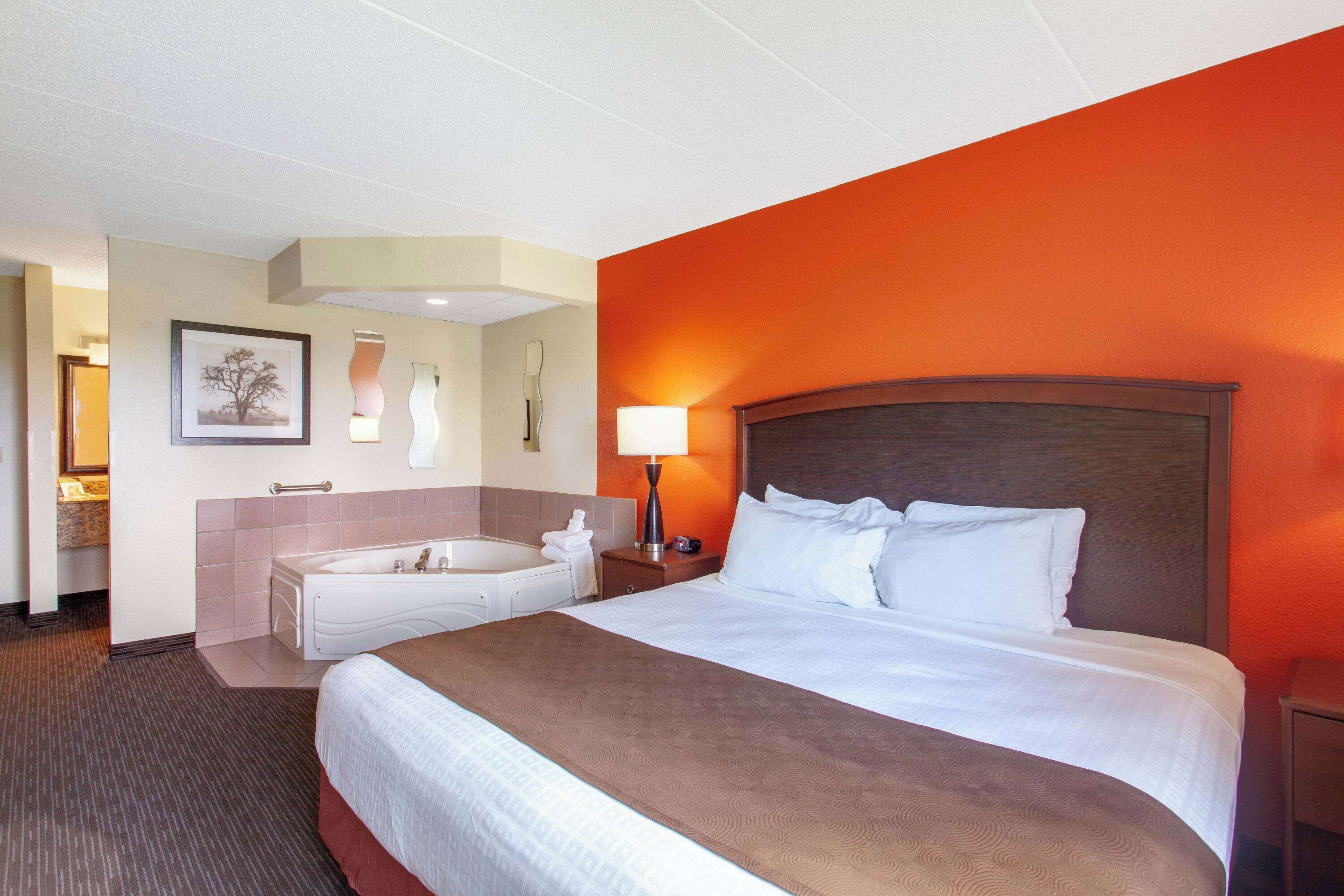 A hotel room with a large bed, a bathroom with a bathtub, and a nightstand with a lamp.
