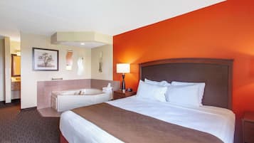 A hotel room with a large bed, a bathroom with a bathtub, and a nightstand with a lamp.