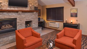 A living room with two orange armchairs, a fireplace, a television, and a window with blinds. - AmericInn by Wyndham St. Cloud MN I-94 (St Cloud)
