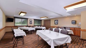 Un salón de conferencias con varias mesas y sillas, equipado con manteles blancos y tazas.