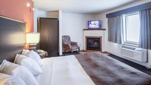 A hotel room with a large bed, a television, a fireplace, and a window with curtains. - Quality Inn Atchison (Atchison)