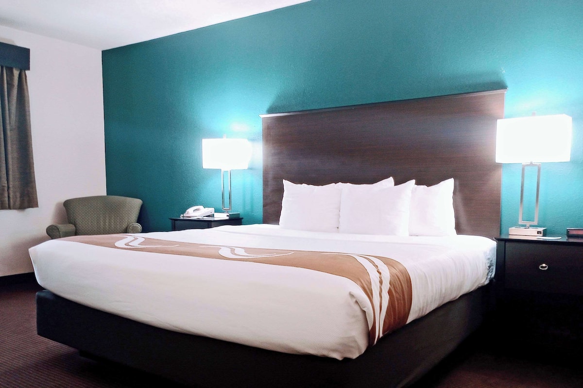 Una habitación de hotel con una cama grande, dos lámparas de noche, un teléfono y una silla.