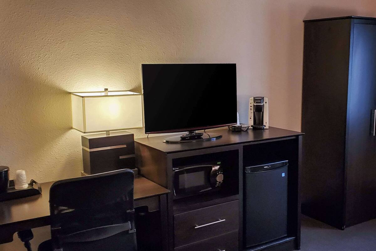 Habitación de hotel compacta con televisión de pantalla plana, un refrigerador pequeño, microondas y un área de descanso.