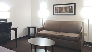 A hotel room with a sofa, a small round table, a desk, and a lamp. - Quality Inn Atchison (Atchison)