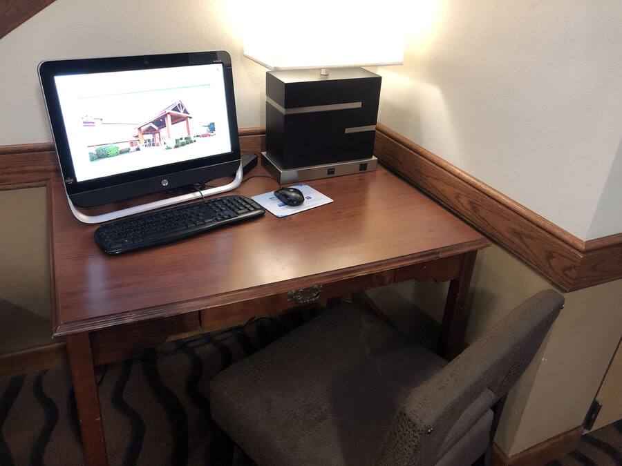A wooden desk with a laptop, keyboard, mouse, and a lamp.