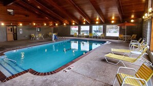 An indoor swimming pool with wooden beams, lounge chairs, and a view of the outside. - Quality Inn Atchison (Atchison)