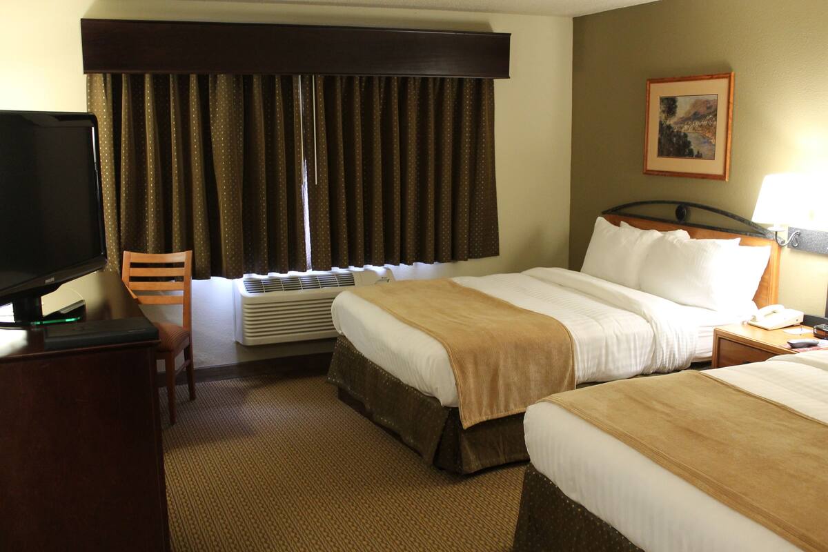 Habitación de hotel con cama, escritorio con computadora, una silla y ventana con cortinas.