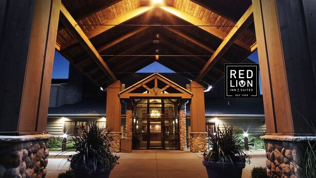 Exterior del Red Lion Inn & Suites con entrada cubierta, pilares de piedra y plantas en macetas.