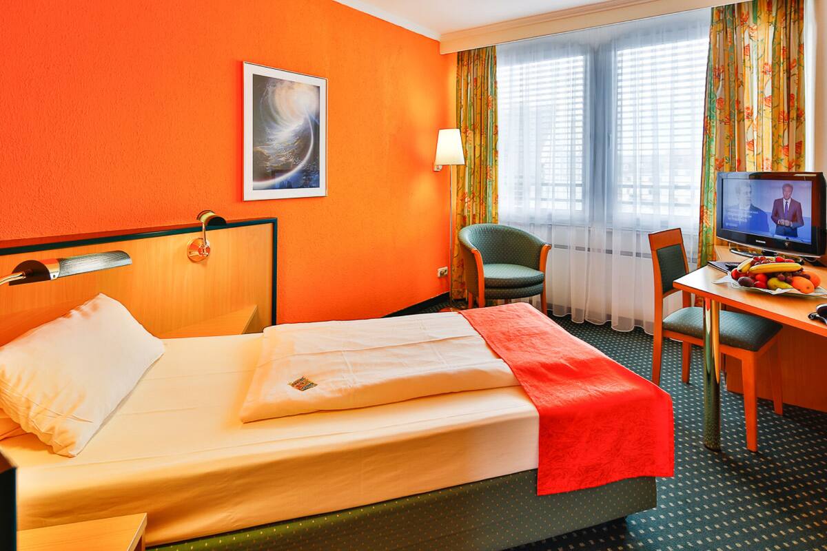 Et hotelværelse med seng, skrivebord med computer, stol og fjernsyn.
