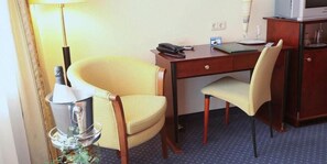 A hotel room with a wooden desk, two chairs, a telephone, a lamp, and a minibar. - Hotel Präsident (Munich)
