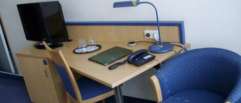 Habitación de hotel con escritorio de madera, computadora, teléfono, lámpara y una silla azul con lunares.