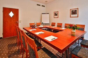 Una sala conferenze con un lungo tavolo, sedie, una lavagna e quadri appesi al muro.