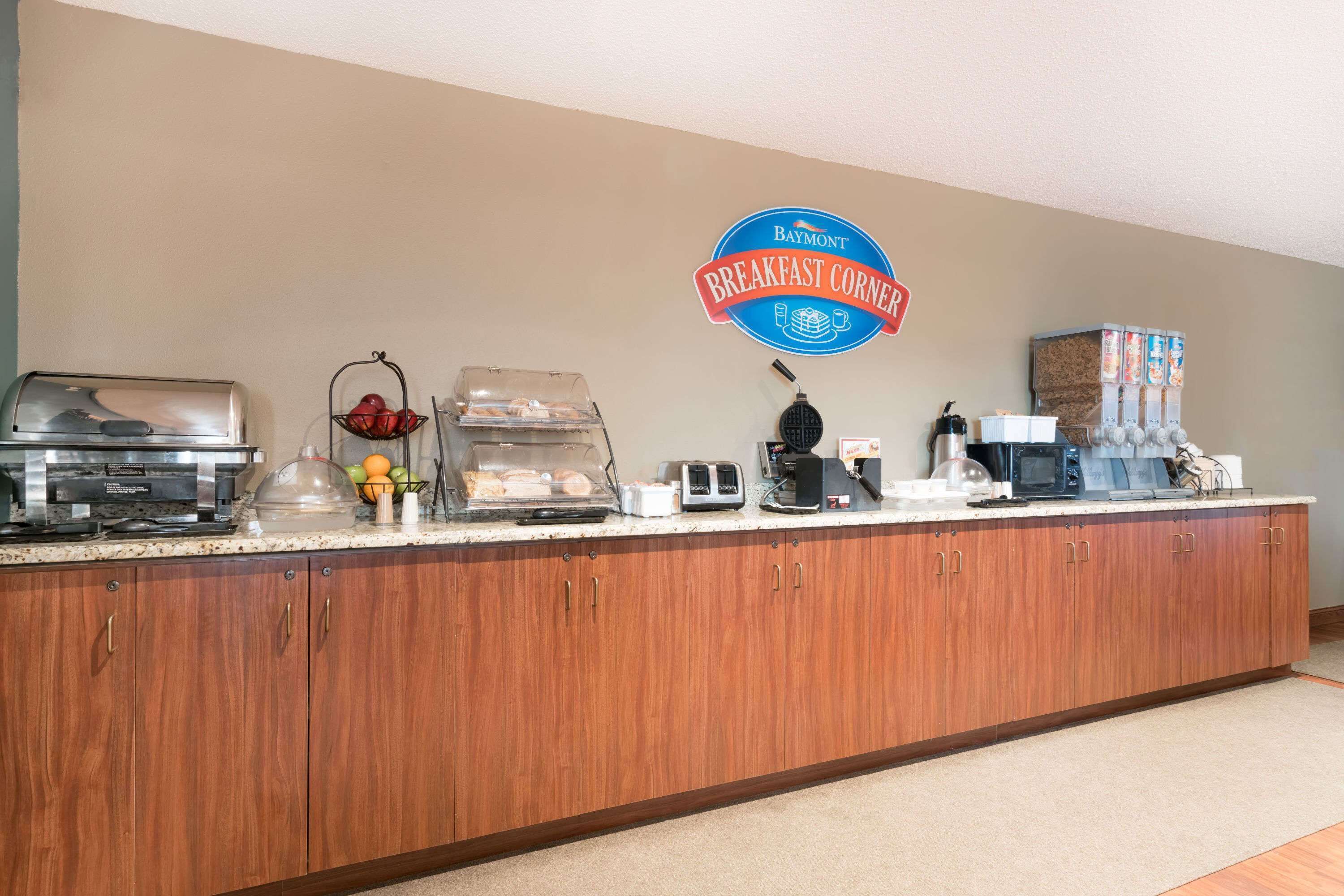 A breakfast station with a Baymont sign, a coffee maker, a microwave, and a fruit bowl.