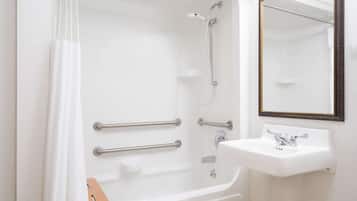 Un baño con bañera, barras de apoyo, ducha, lavamanos y espejo.