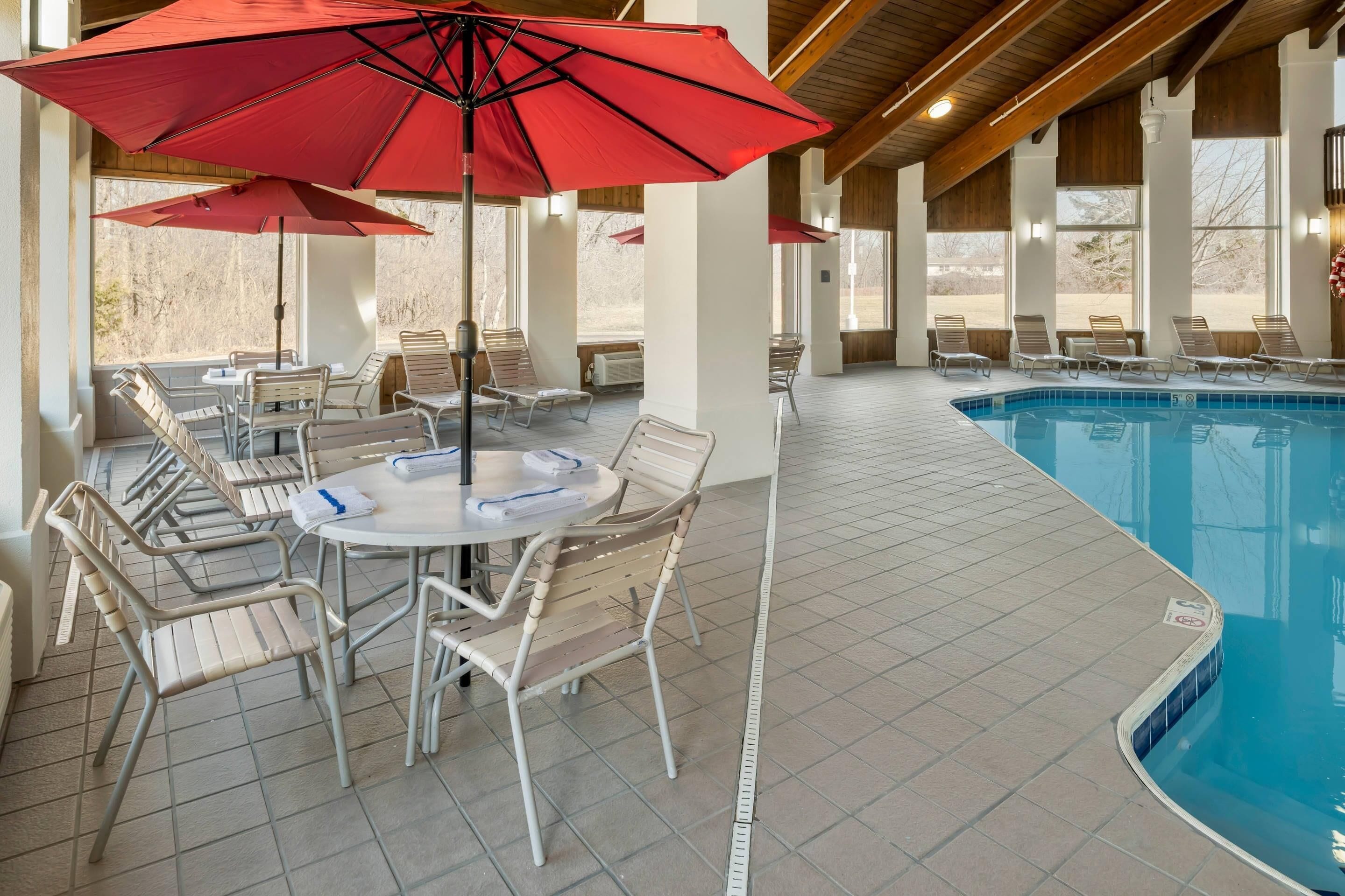 A poolside area with lounge chairs, a table with chairs, and red umbrellas.