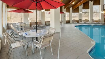 A poolside area with lounge chairs, a table with chairs, and red umbrellas.