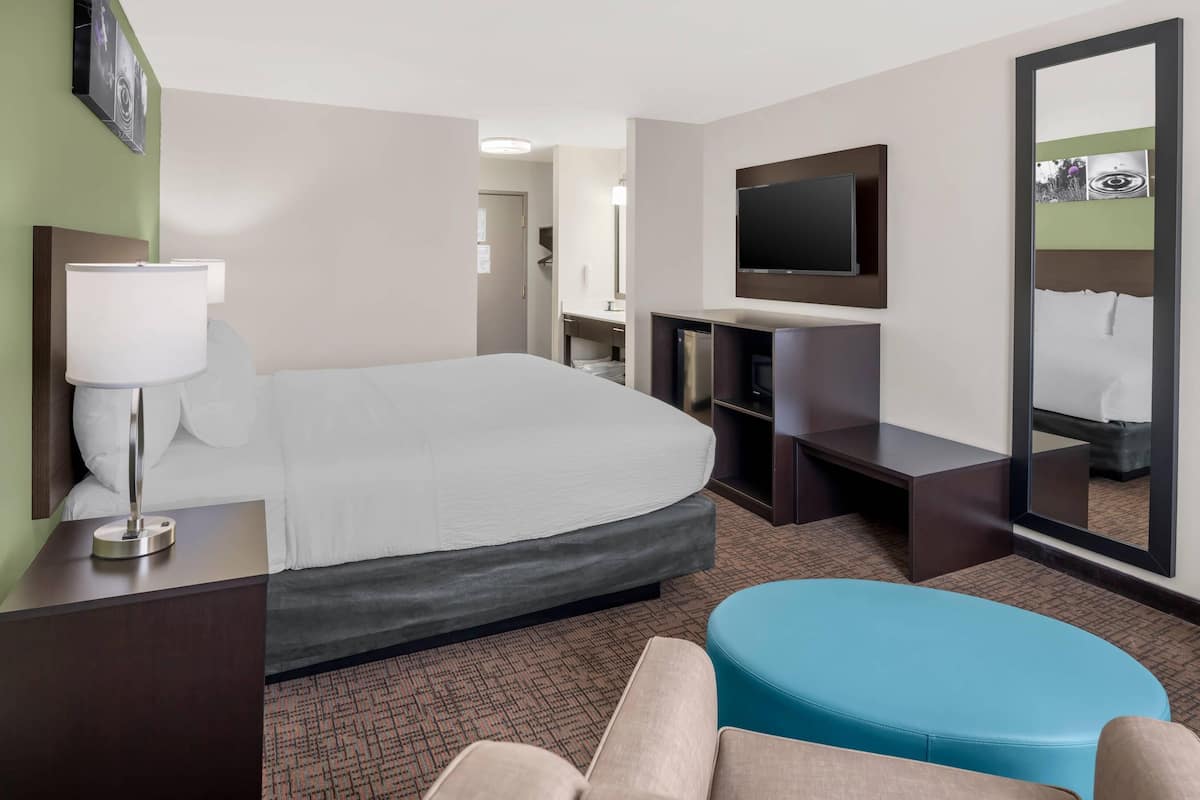 Habitación de hotel con cama, televisor, escritorio con lámpara, espejo y zona de estar.