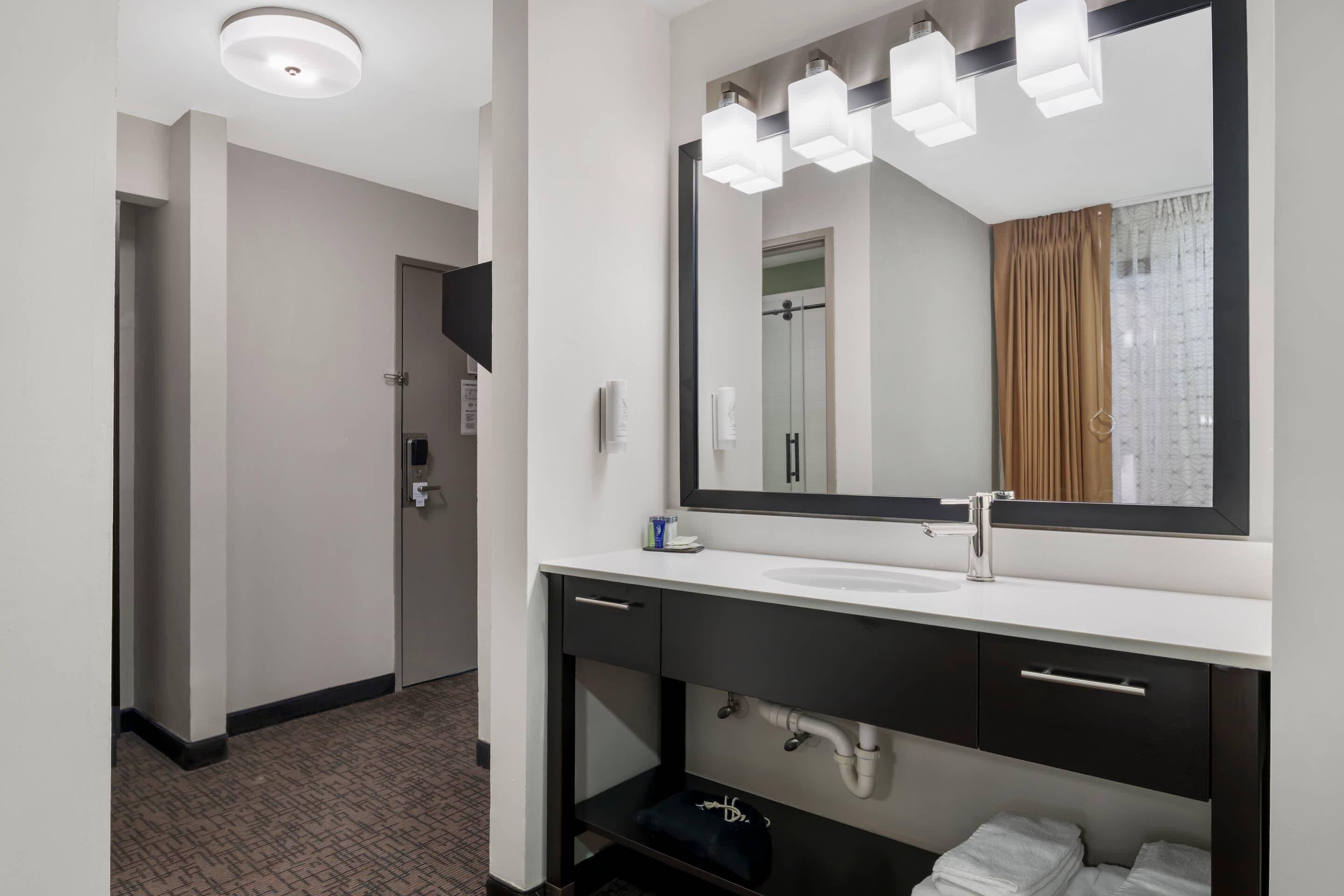 A modern bathroom with a white sink, dark vanity, and a large mirror with lights.