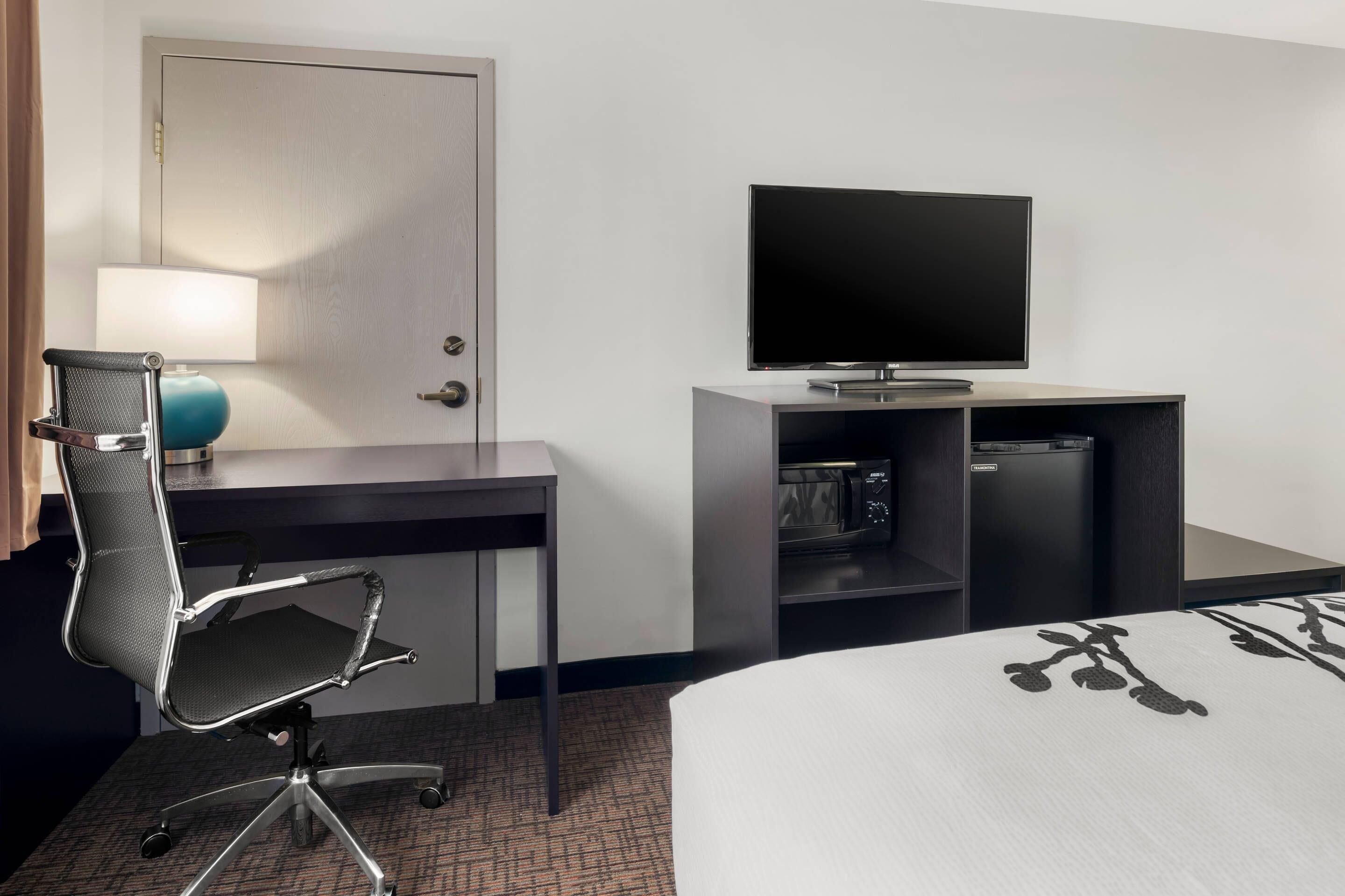 Une chambre d’hôtel comprenant un lit, un bureau avec une chaise, une télévision, un four à micro-ondes et une porte.
