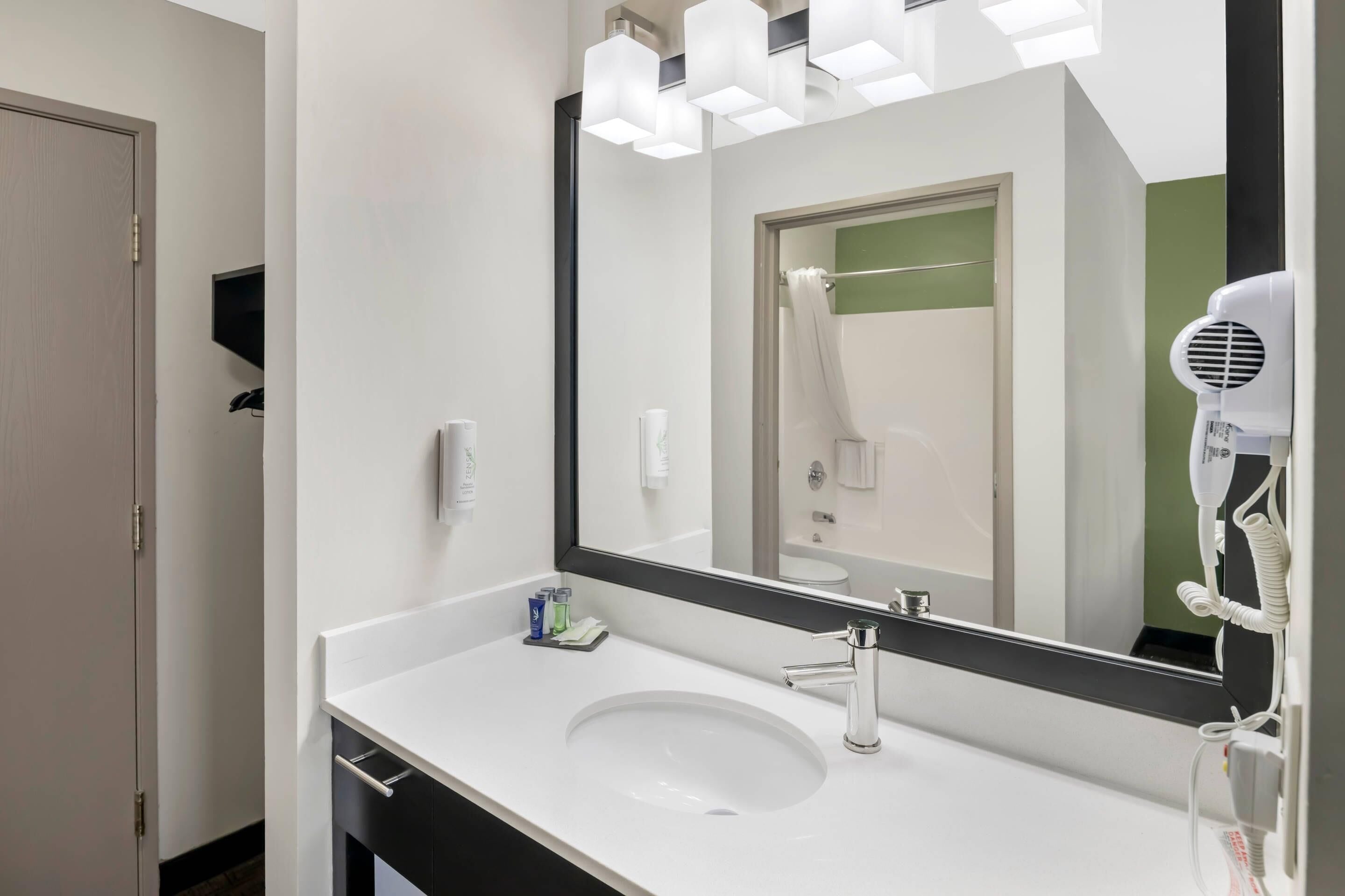 A modern bathroom with a white sink, a large mirror, and a hairdryer mounted on the wall.