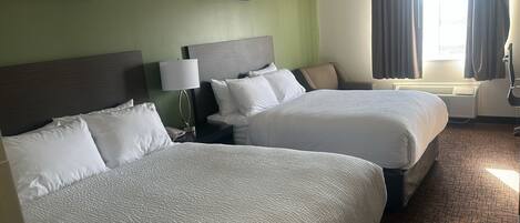 Habitación de hotel con dos camas, una mesita de noche con lámpara y una ventana con cortinas.