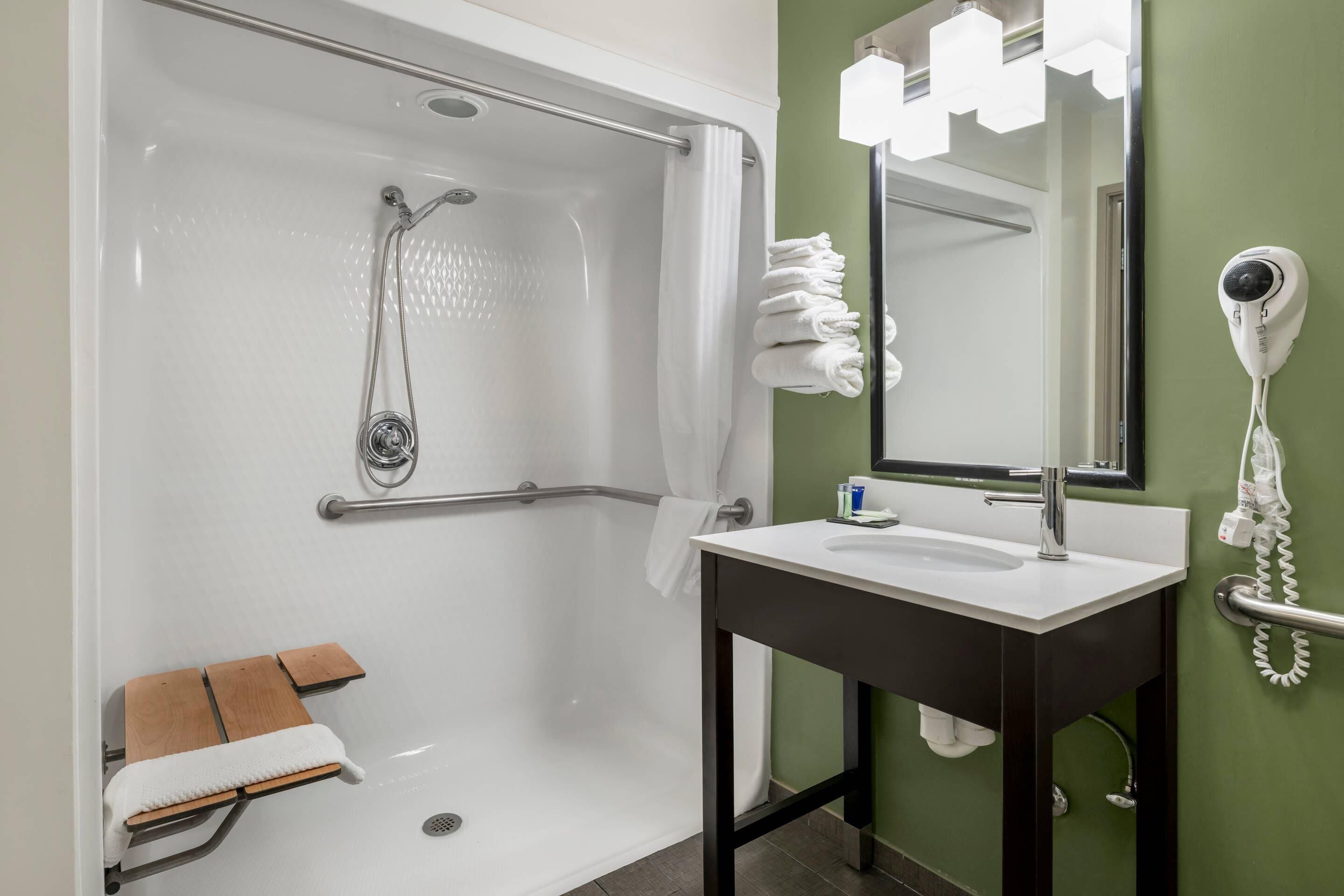 A bathroom with a shower, a sink, a mirror, a hairdryer, and a towel rack.