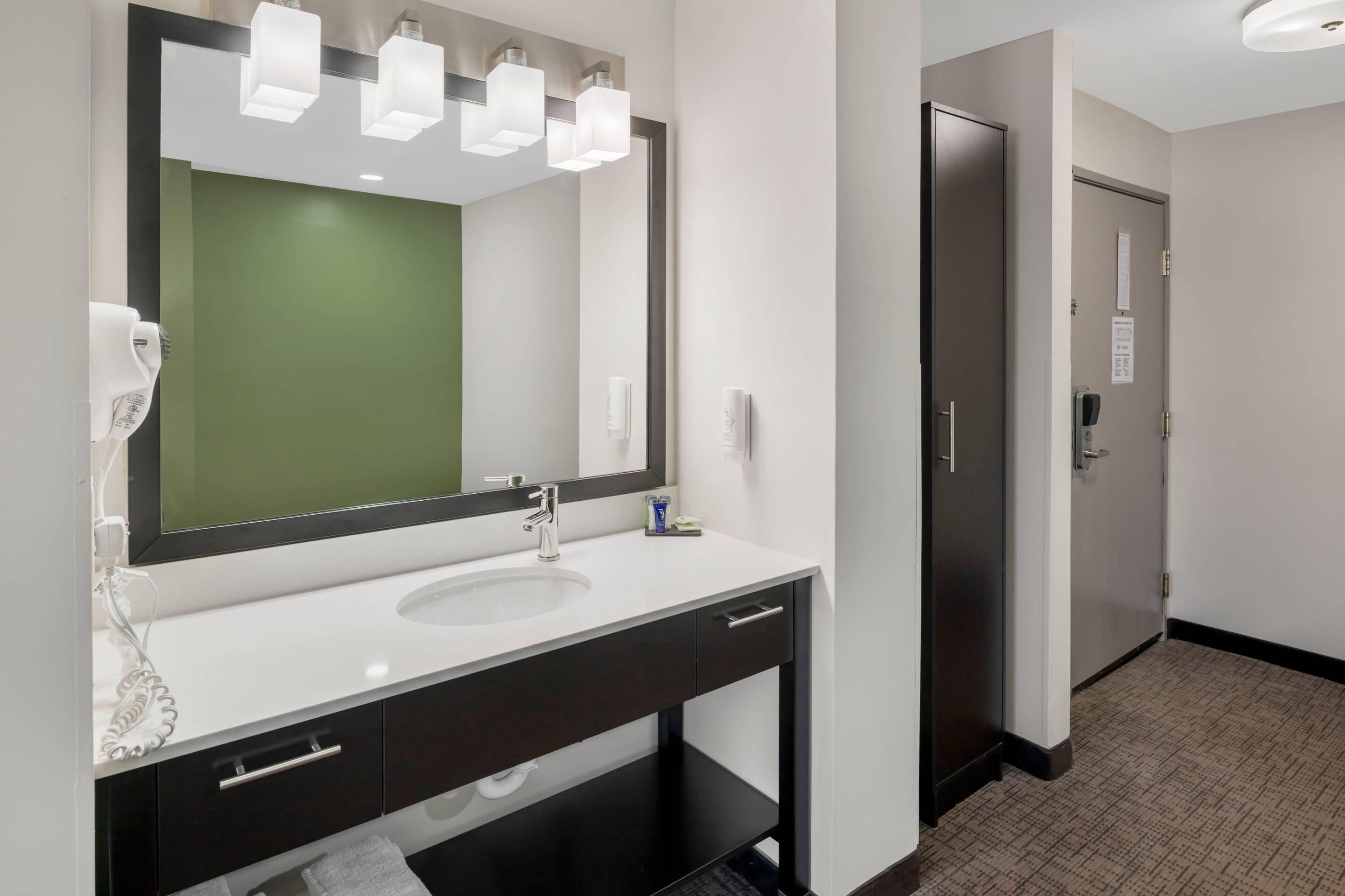 A modern bathroom with a large mirror, a white sink, and a dark vanity.