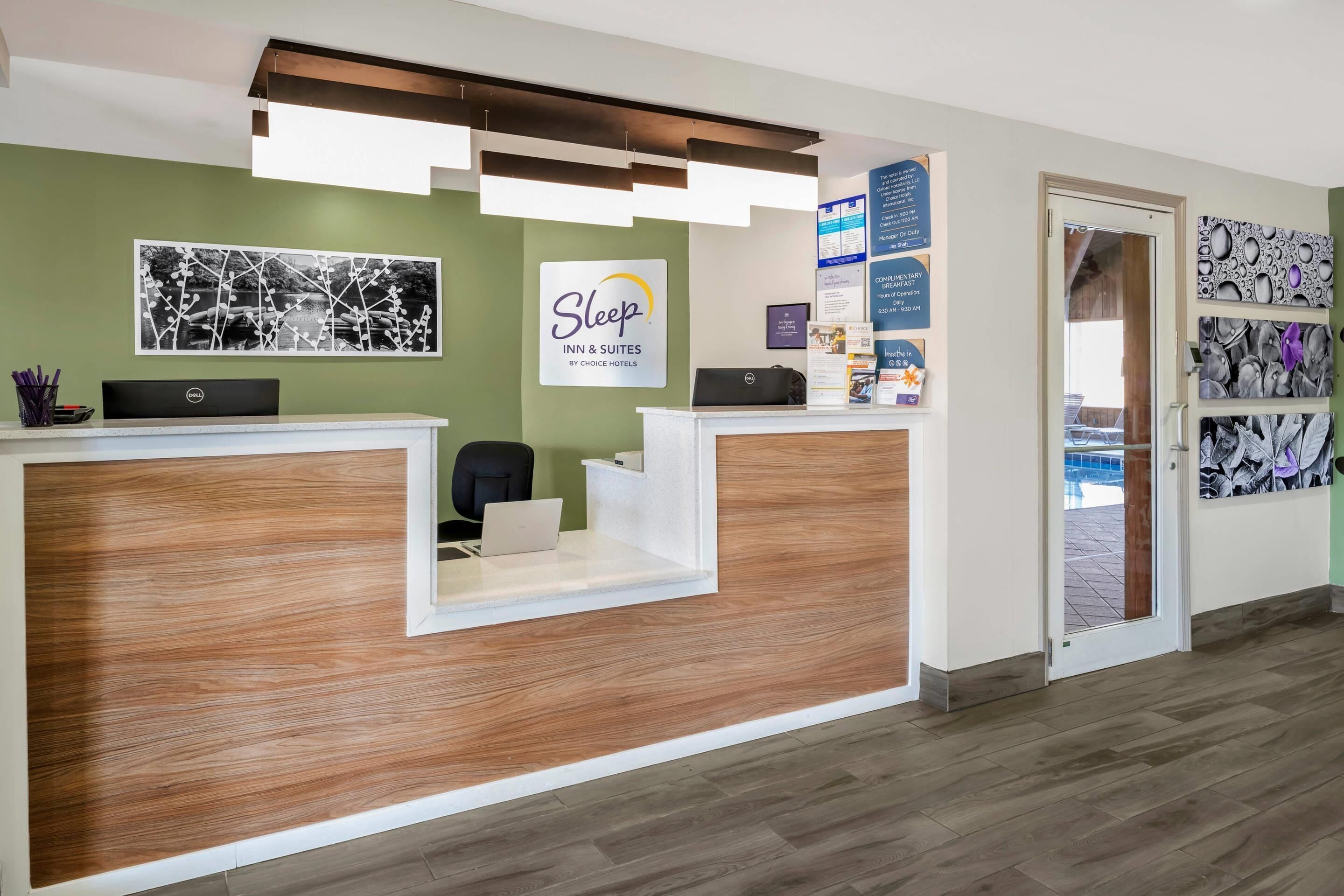 A reception desk with a sign for Sleep Inn & Suites by Choice Hotels, a laptop, and informational brochures on the wall.