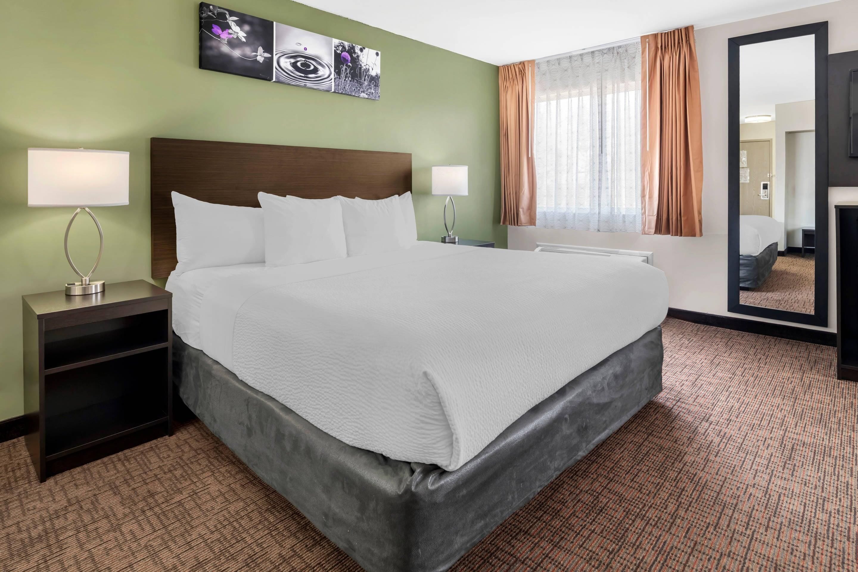 Habitación de hotel con una cama grande, dos mesitas de noche con lámparas, un espejo y una obra de arte en la pared.