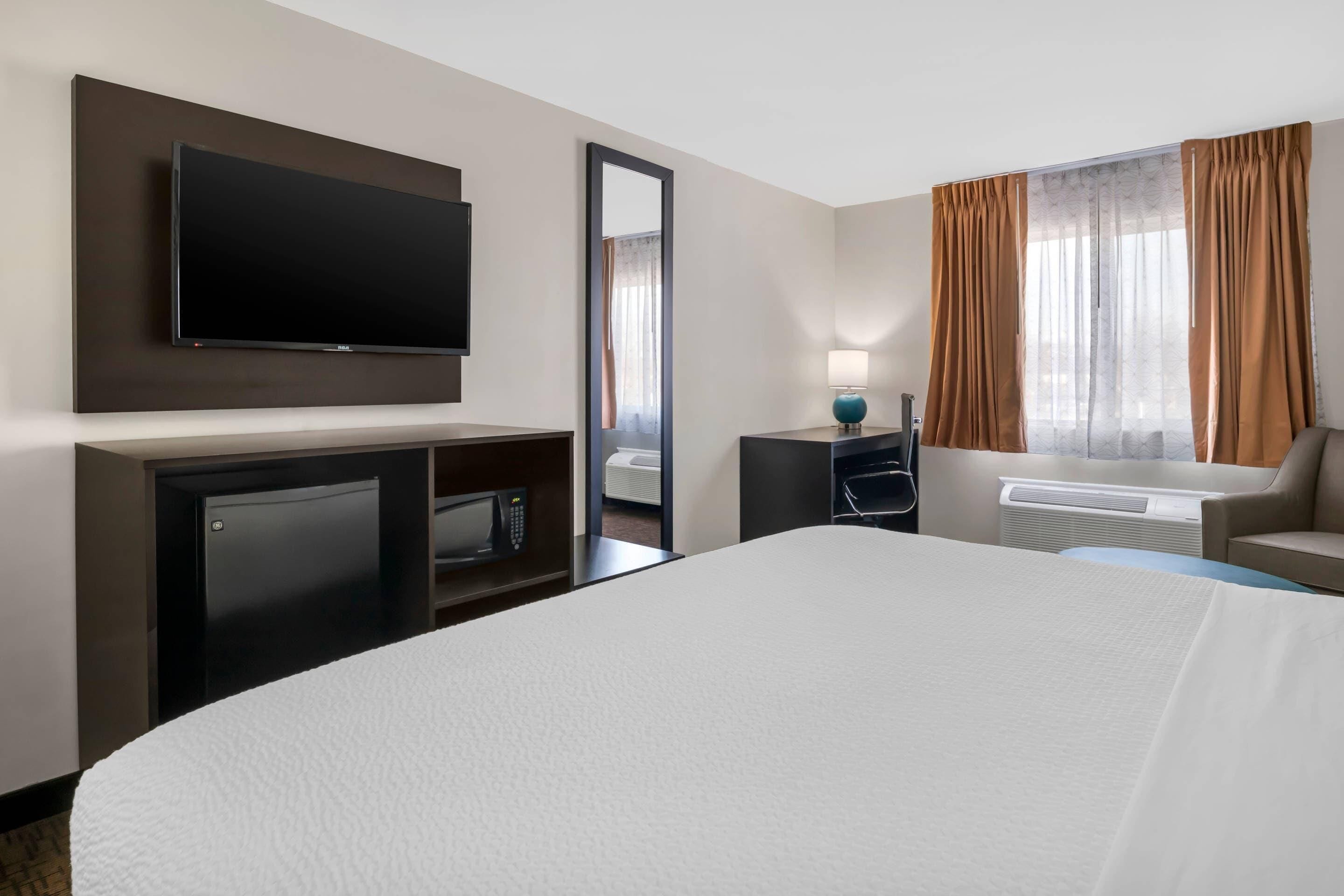 Habitación de hotel con cama, televisión, escritorio con lámpara, una silla y ventana con cortinas.