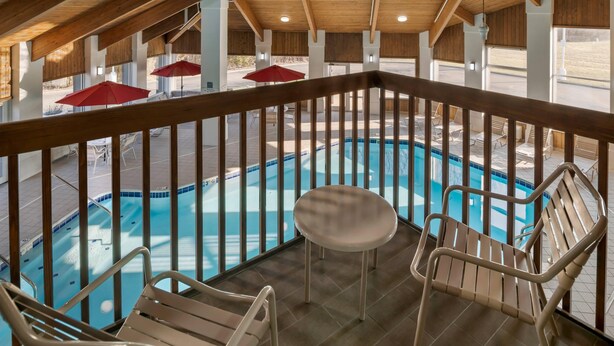 A poolside area with a wooden deck, lounge chairs, and umbrellas.