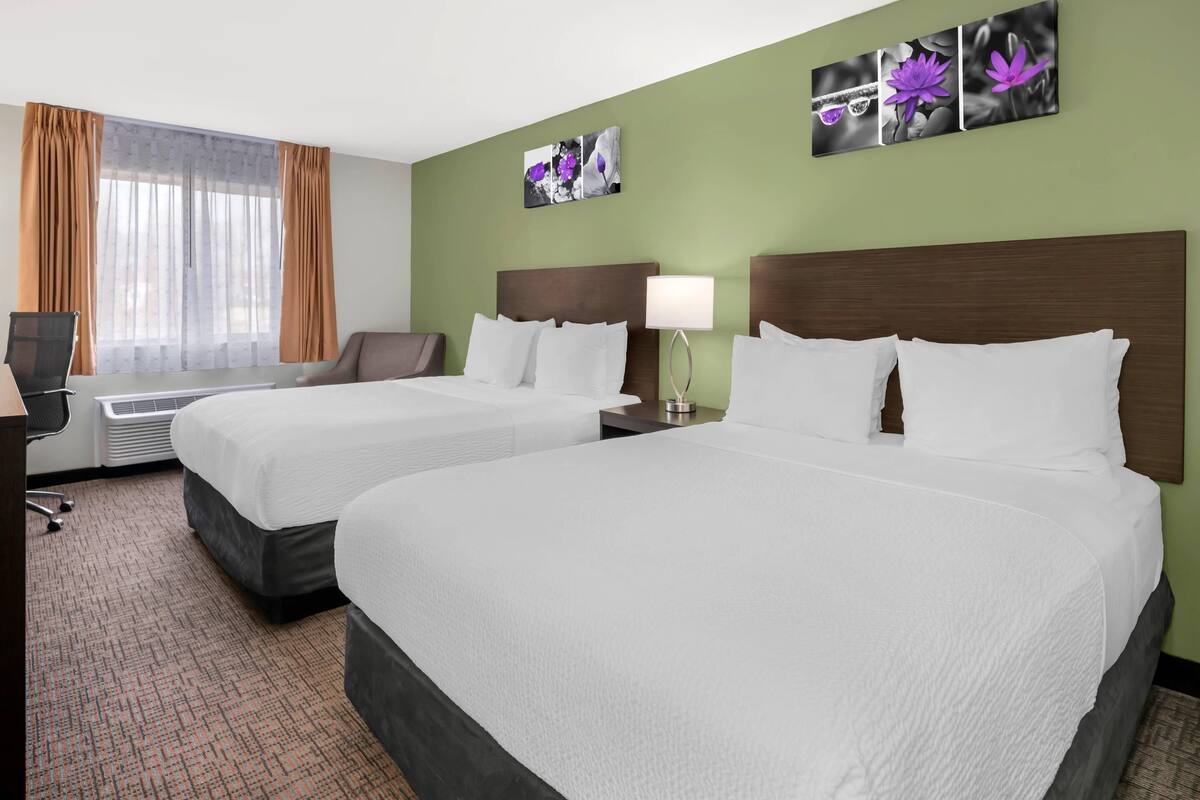 Habitación de hotel con dos camas, un escritorio, una silla, una lámpara y cuadros en la pared.