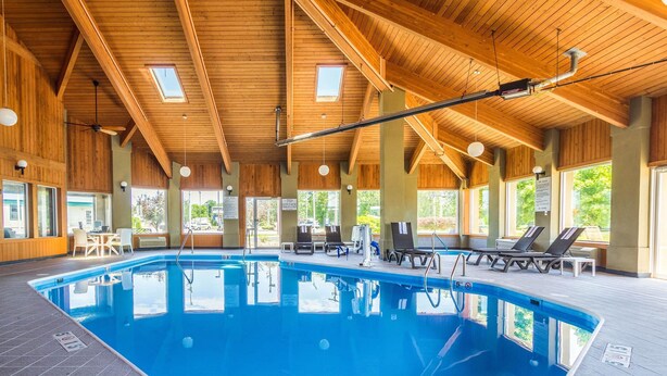 An indoor swimming pool with wooden beams, lounge chairs, and a view of the outdoors. - Comfort Inn Norwalk - Sandusky (Norwalk)