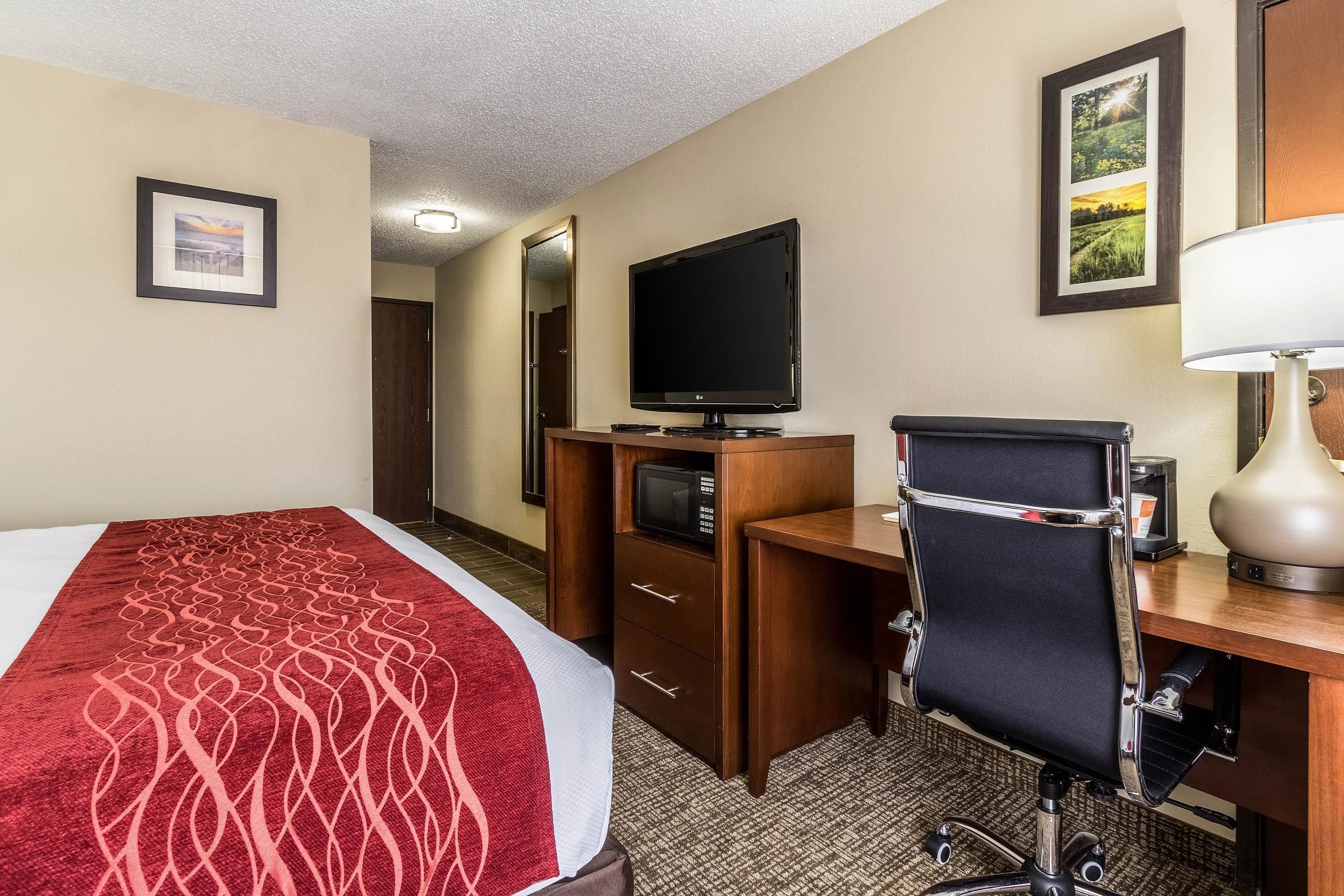 A hotel room with a bed, a desk with a computer, a television, and a lamp.
