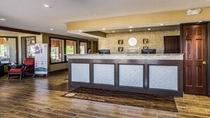 A reception area with a wooden floor, a reception desk, a red chair, and framed pictures on the wall. - Comfort Inn Norwalk - Sandusky (Norwalk)
