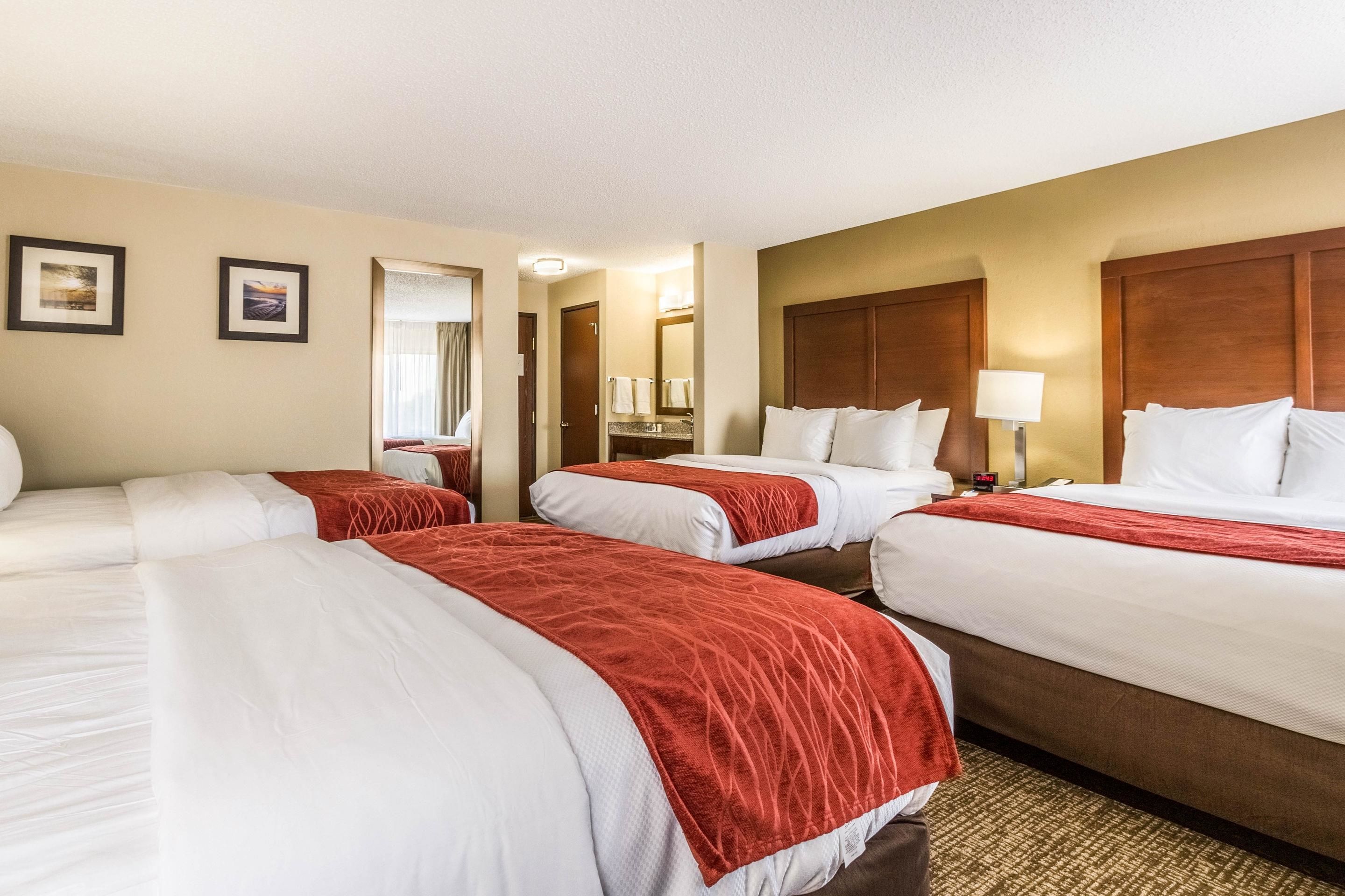 A hotel room with four beds, a large mirror, and a nightstand with a lamp.