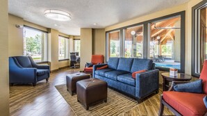 A spacious lobby with a blue sofa, red armchairs, and a small table. Large windows offer views of the outdoors. - Comfort Inn Norwalk - Sandusky (Norwalk)