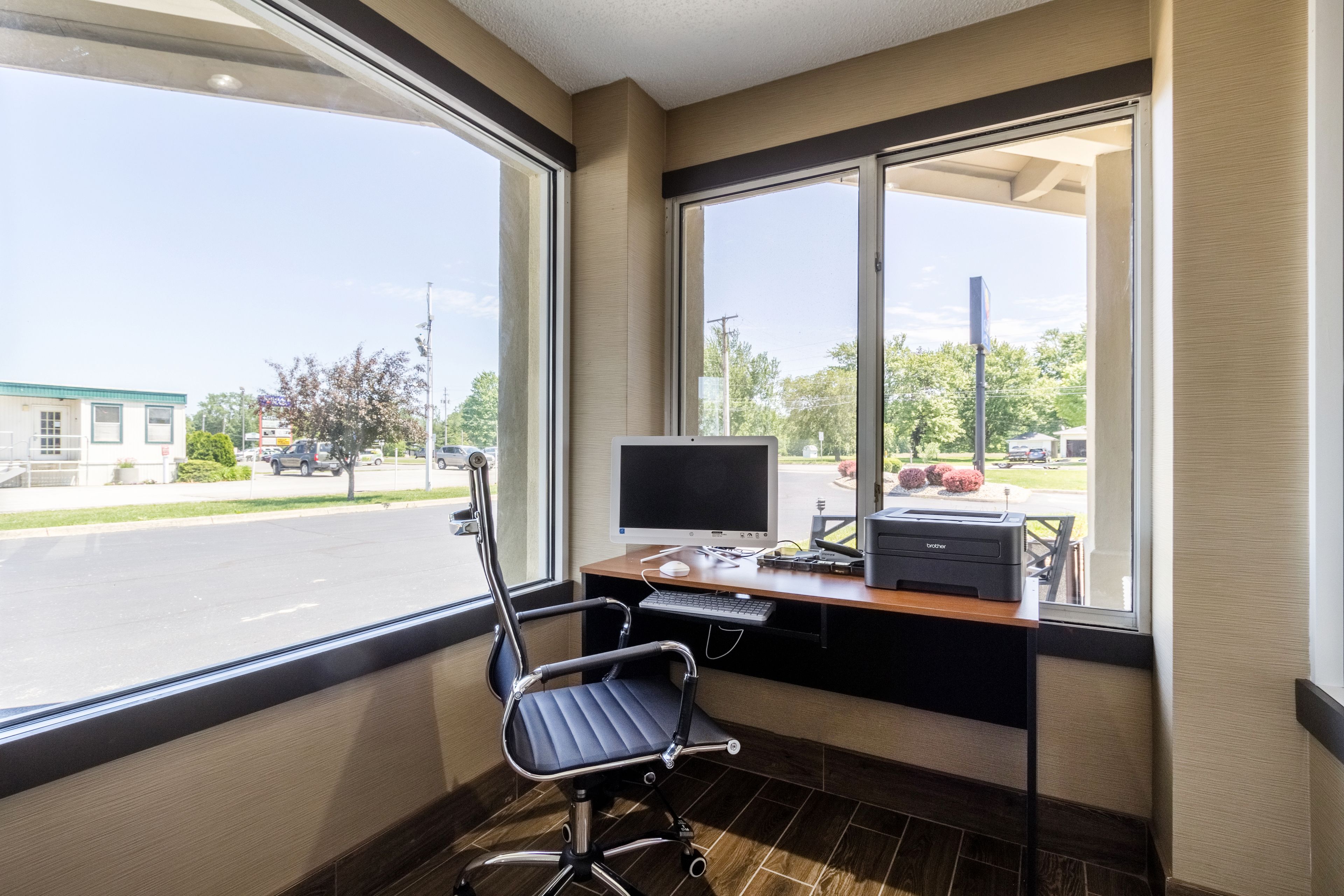 Espaço de escritório moderno com mesa, computador e cadeira, grandes janelas com vista para a rua.