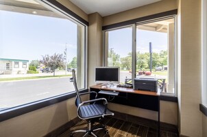 Espaço de escritório moderno com mesa, computador e cadeira, grandes janelas com vista para a rua.