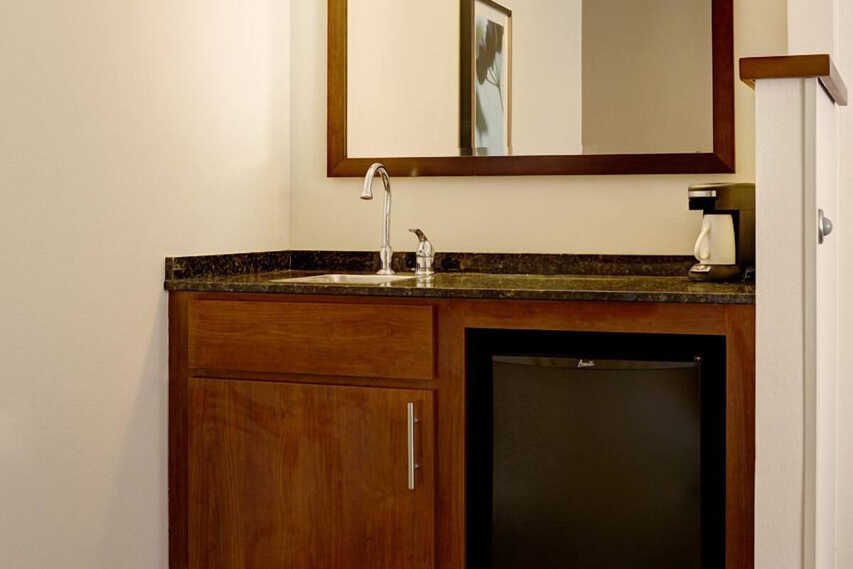 Een hotelbadkamer met een houten wastafelmeubel, een wastafel, een spiegel en een inbouw medicijnkast.