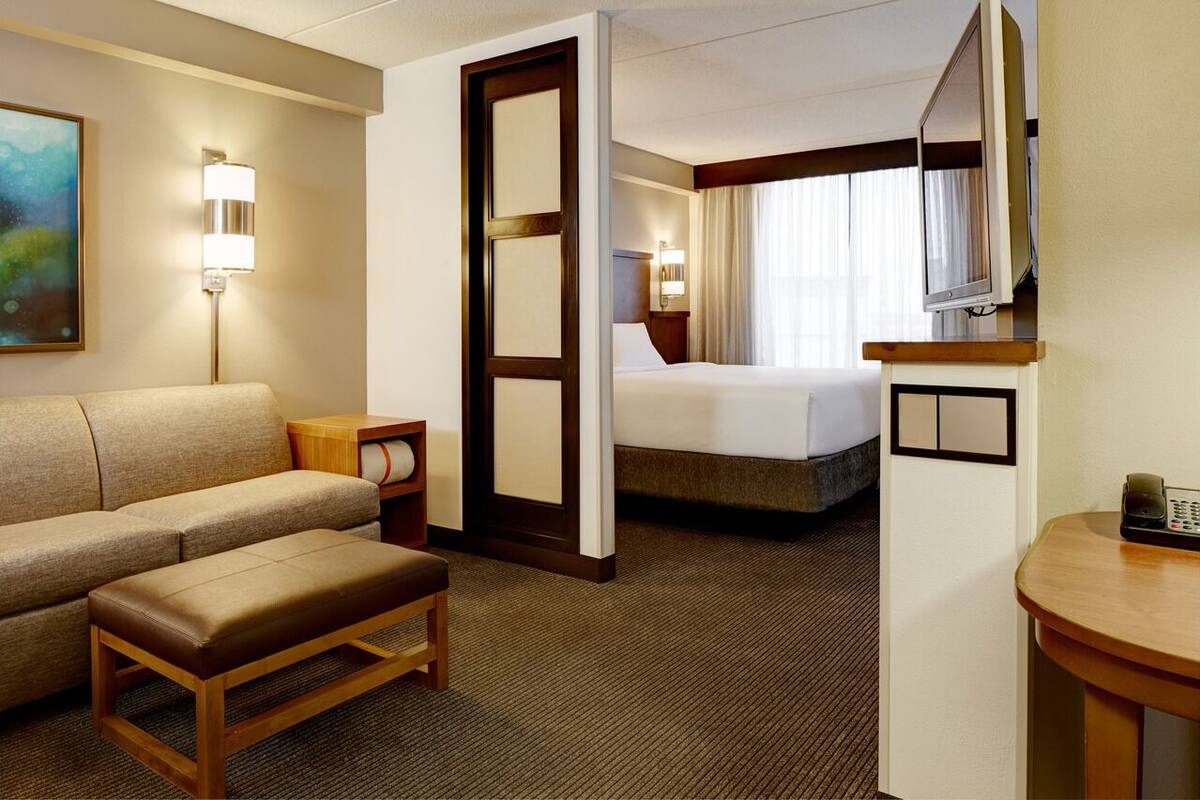 Een hotelkamer met een bed, een bank, een kleine tafel, een televisie en een schilderij aan de muur.