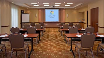 A conference room with a large screen displaying the Hyatt Place logo, multiple tables with chairs, and a carpeted floor.