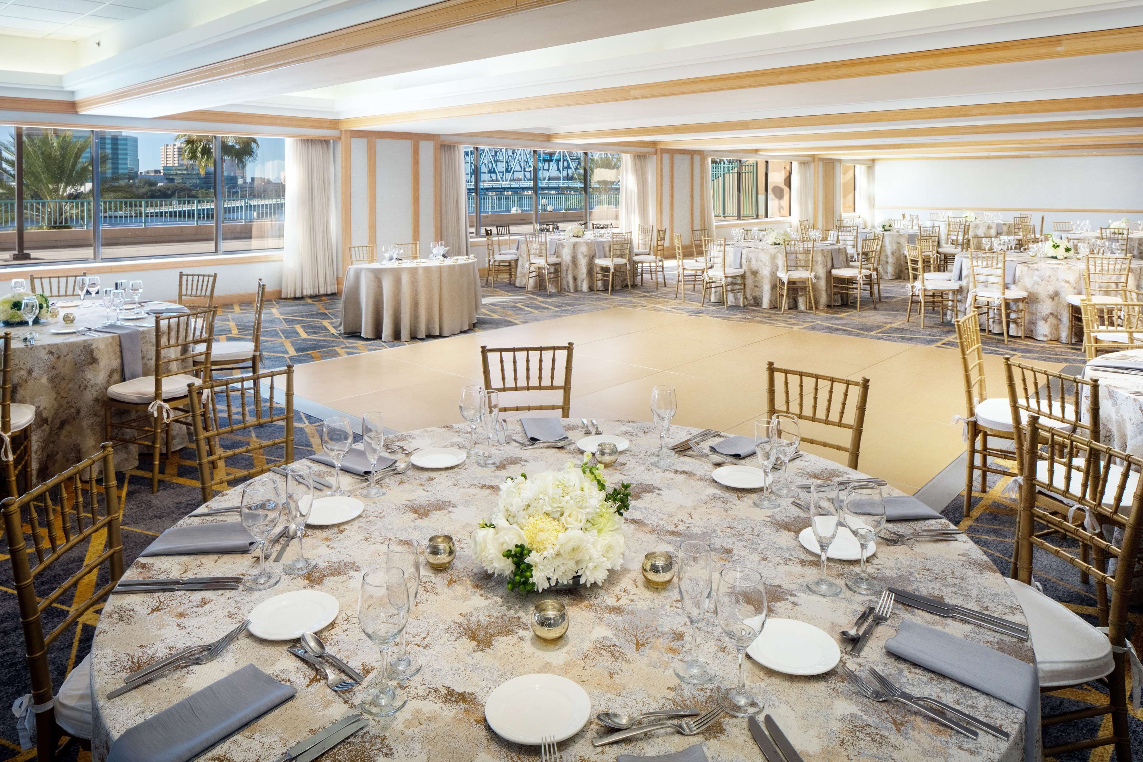 A banquet hall with round tables set for dining, featuring white tablecloths and gold centerpieces.