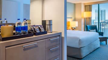 Ein Hotelzimmer mit Bett, Schreibtisch, Kaffeemaschine, Wasserflaschen und Minibar.