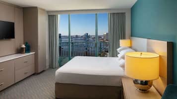 Habitación de hotel con una cama grande, un televisor, un escritorio con lámpara y vistas a la ciudad.