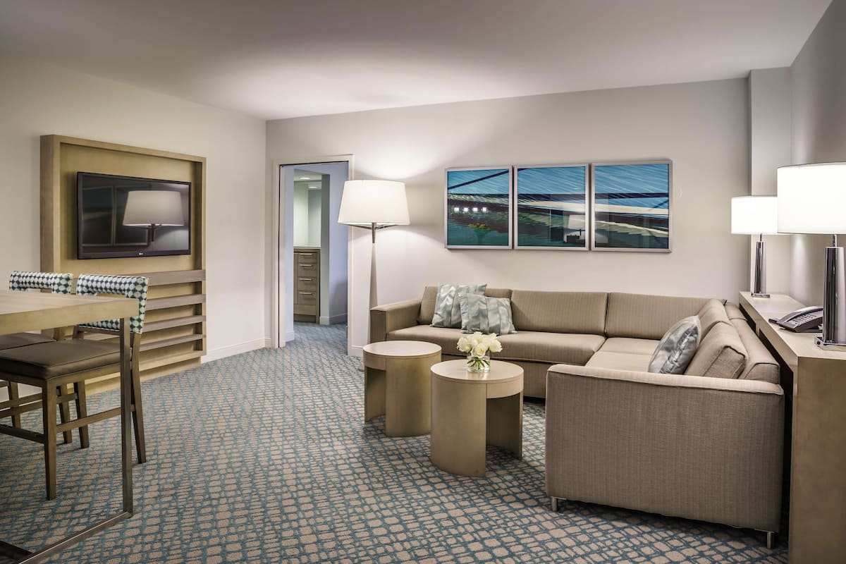 A hotel room with a sofa, two side tables, a TV, and artwork on the wall.